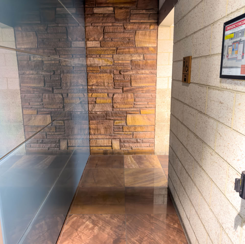 A hallway with a stone wall on the left, a wooden wall on the right, and a polished floor. A framed picture is mounted on the right wall.
