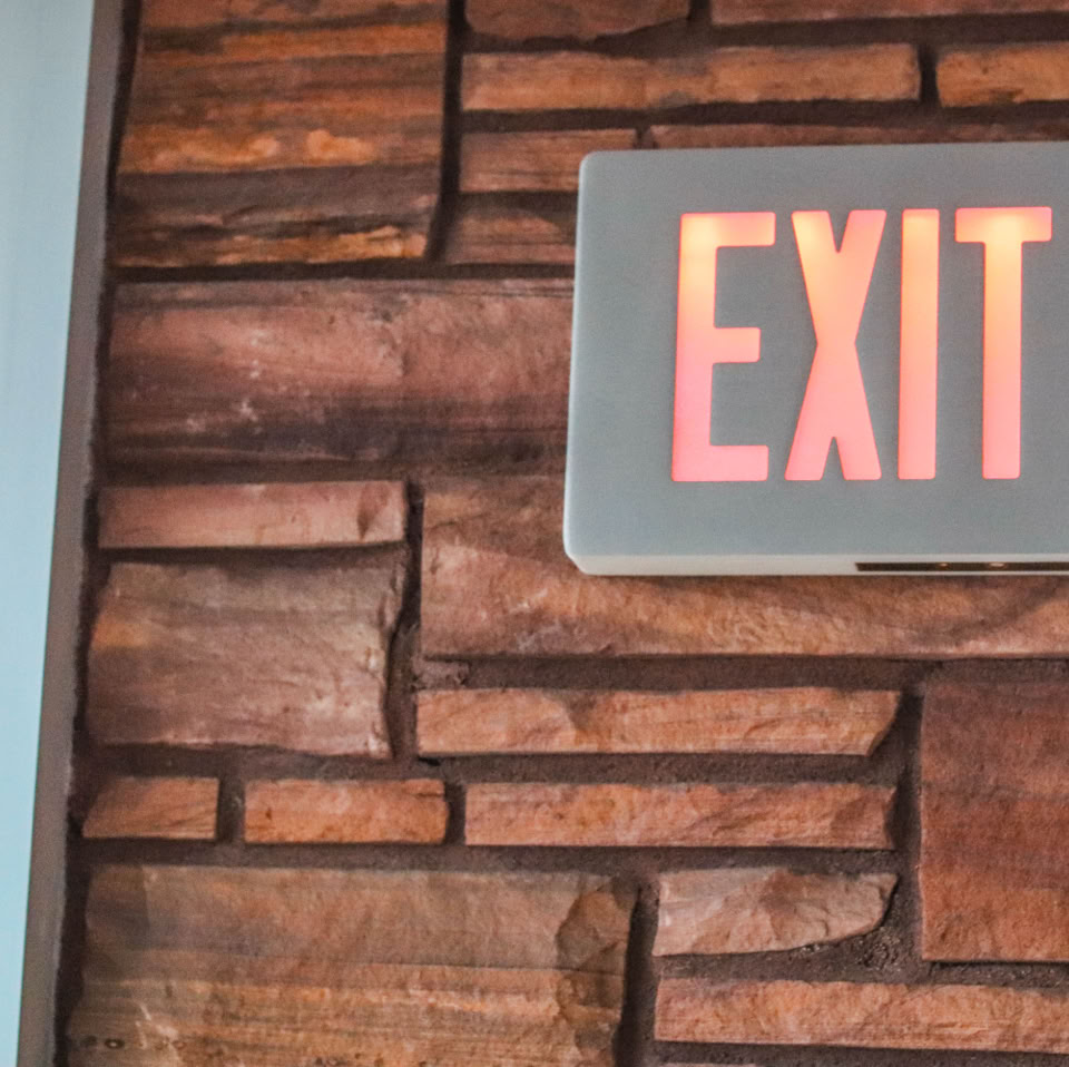 A red "EXIT" sign mounted on a brick wall next to a door.