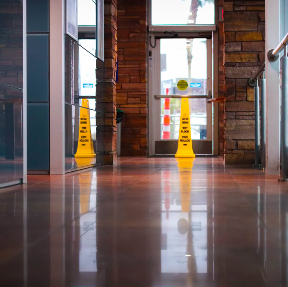 A hallway with polished floors, glass walls, and a yellow caution sign in the center.