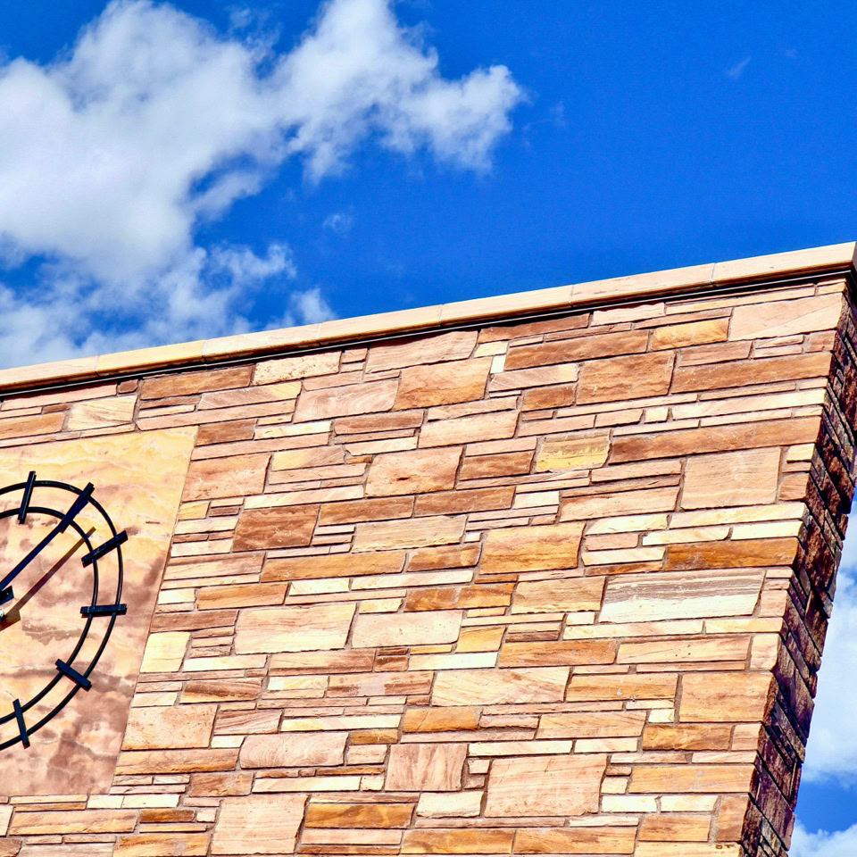 Brick wall with a clock and a blue sky with clouds in the background.