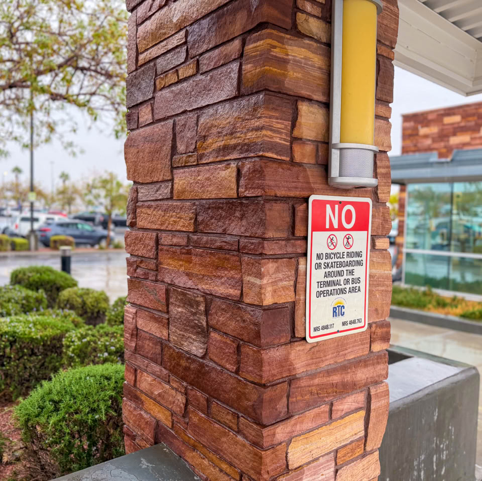 A brick pillar with a "No Smoking" sign, surrounded by greenery and a glass building in the background.