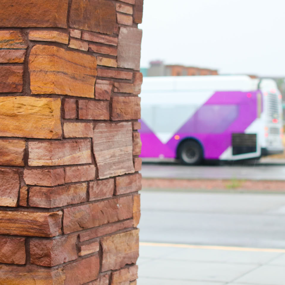 A stone pillar in the foreground with a blurred view of a purple and white bus in the background.