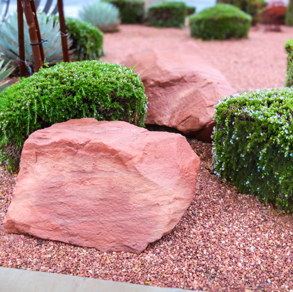 Desert landscape with red rocks, green shrubs, and gravel ground cover.