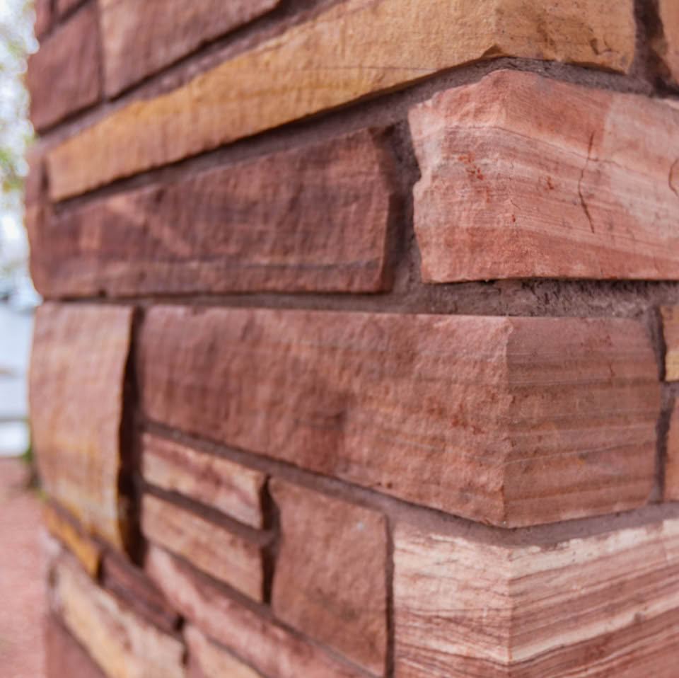 Close-up of a wall made of stacked, rectangular reddish-brown stones with visible layers and textures.