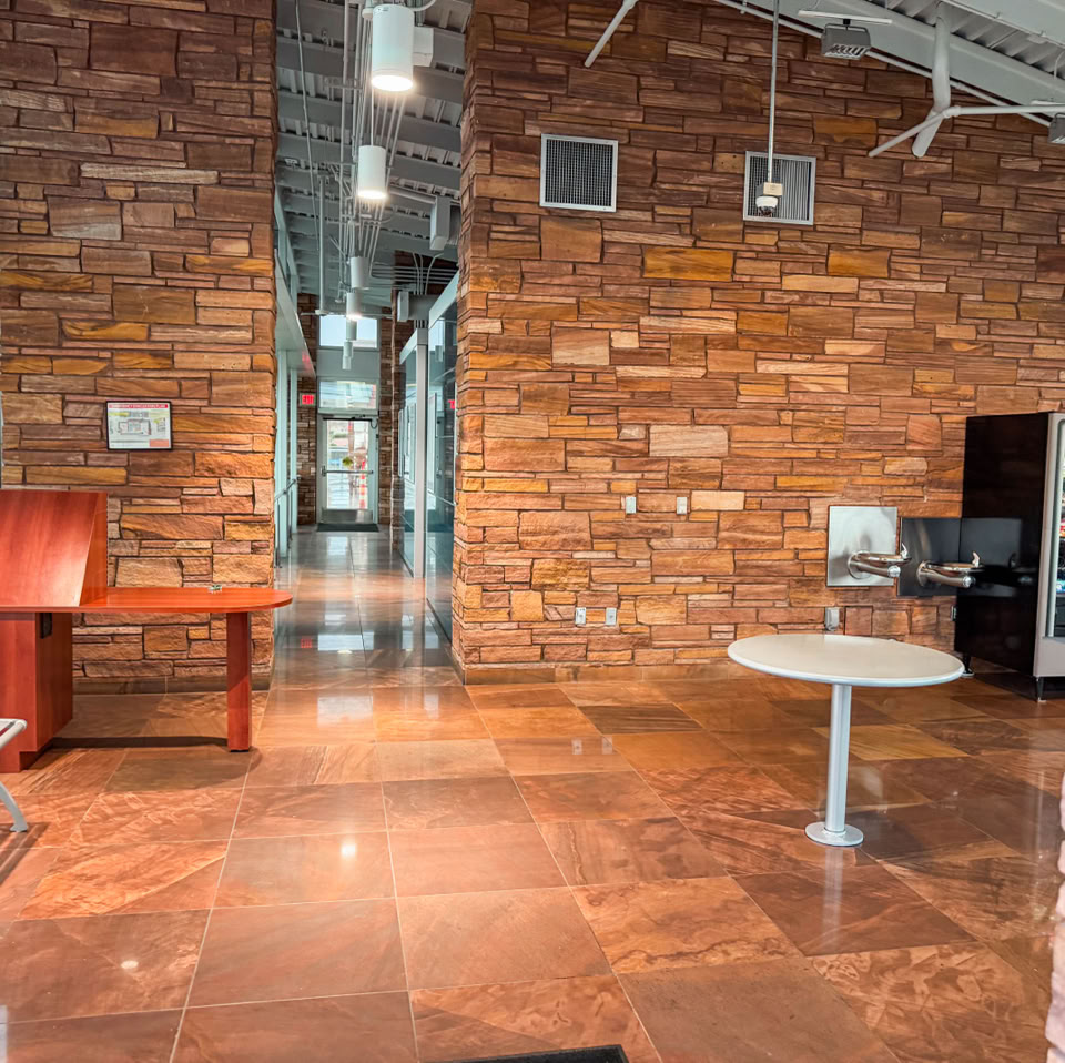 Interior of a room with stone walls, a tiled floor, a wooden table, a round table, and a vending machine.
