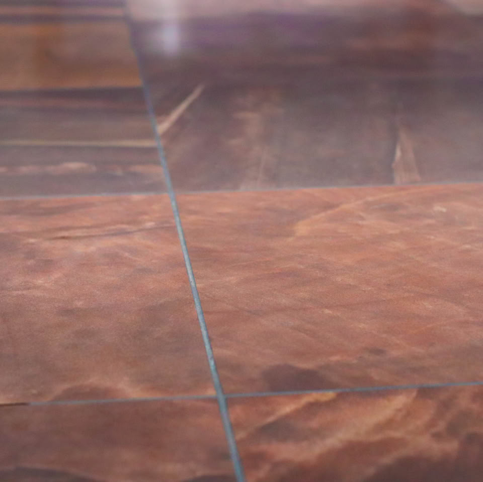 A close-up of a polished wooden surface with visible grain patterns and a reflective sheen.