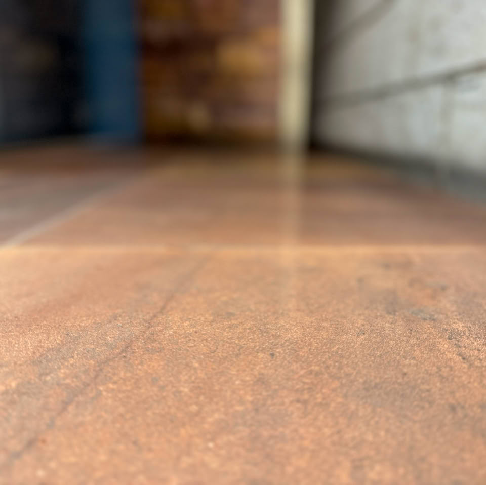 Blurred image of a wooden floor with a brick wall on the left and a concrete wall on the right.