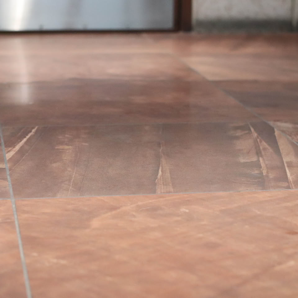 Brown tiled floor with a slightly reflective surface and a blurred background.