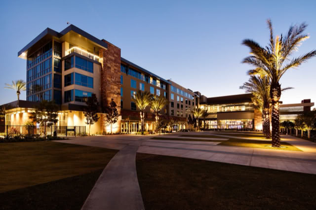 A modern multi-story building with large windows, surrounded by palm trees and illuminated at dusk. at Viejas Casino