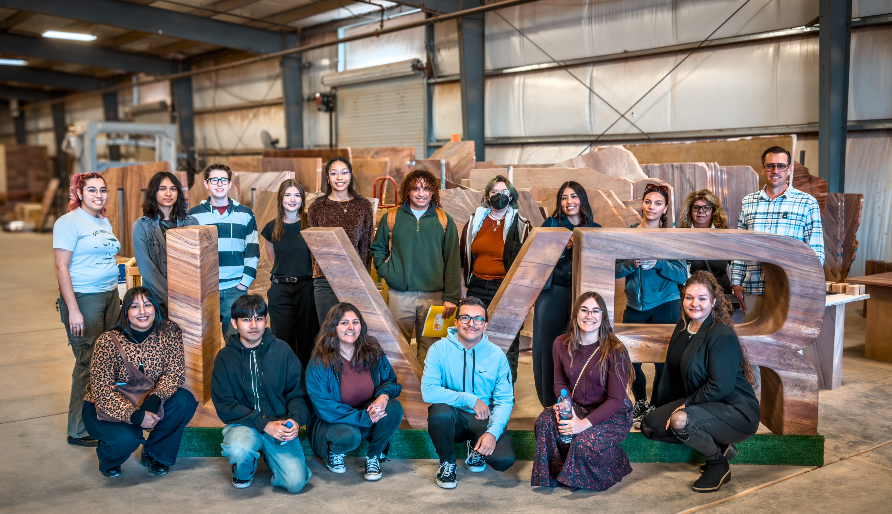 Teachers Workshop Tour people standing around in a factory with hardhats on as one man stands on the podium pointing out different equipment.