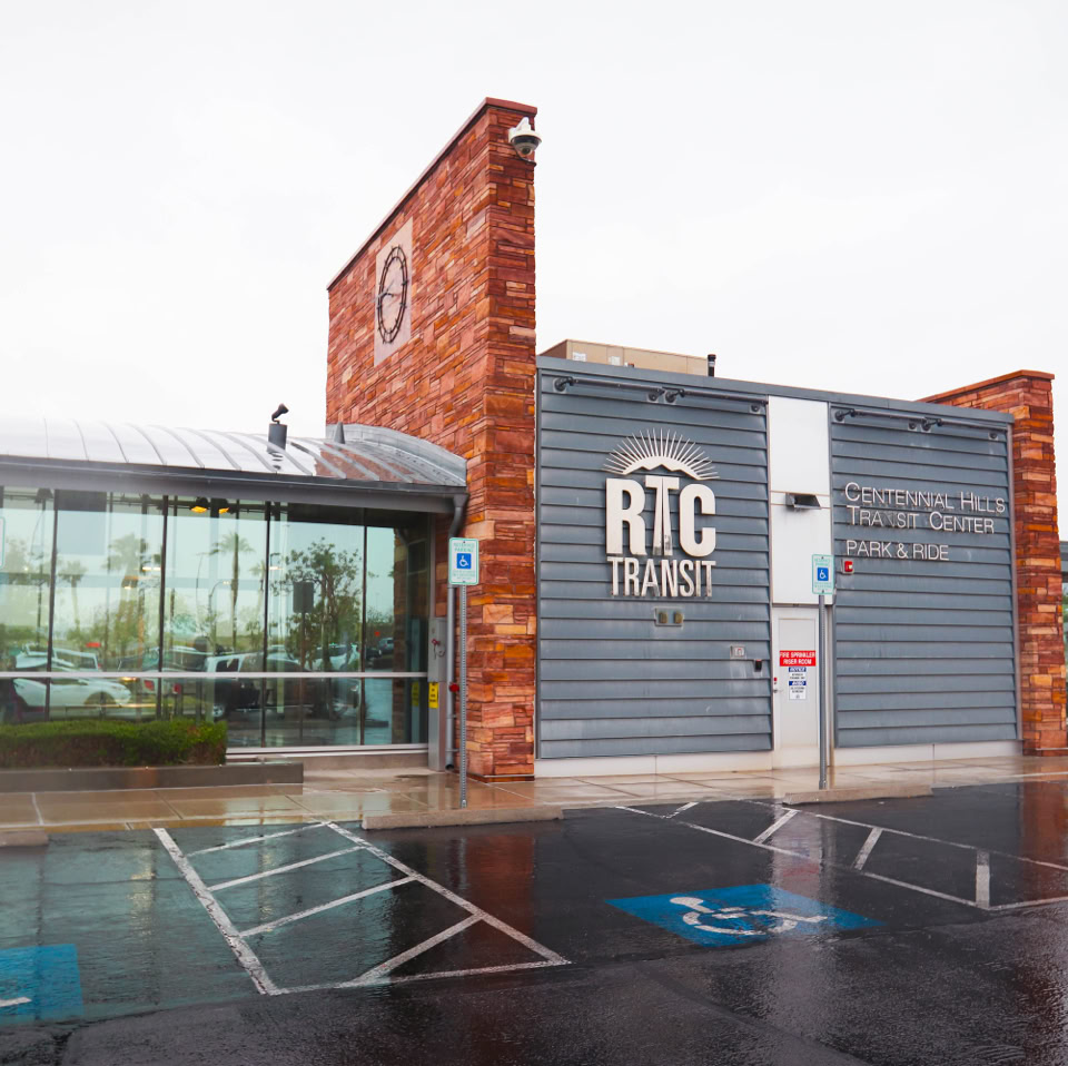 Modern building with glass and brick facade, featuring the letters "RTC" on the side, with a wet parking lot in the foreground.