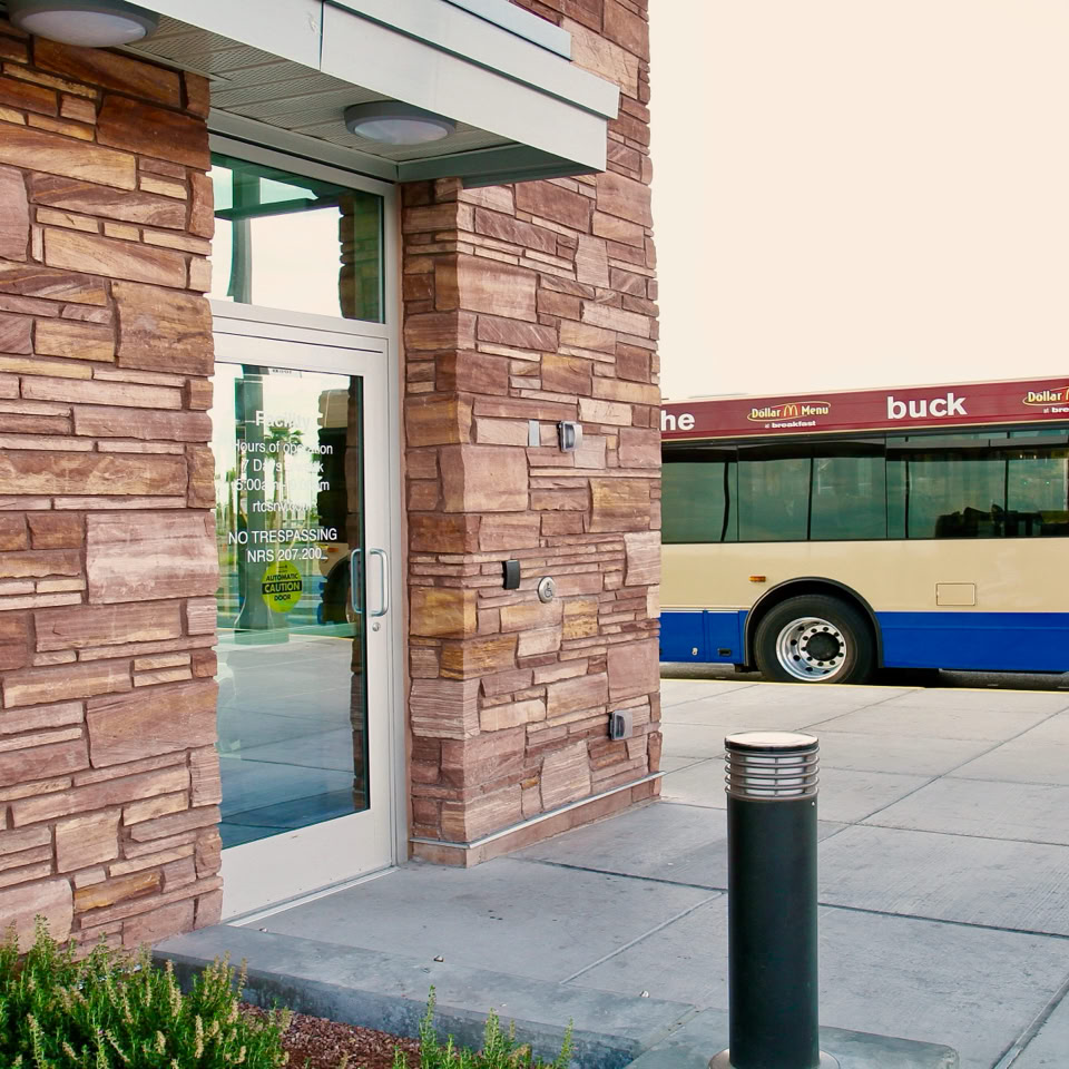 A building with stone walls and a glass door is on the left, and a blue and white bus is parked on the right.