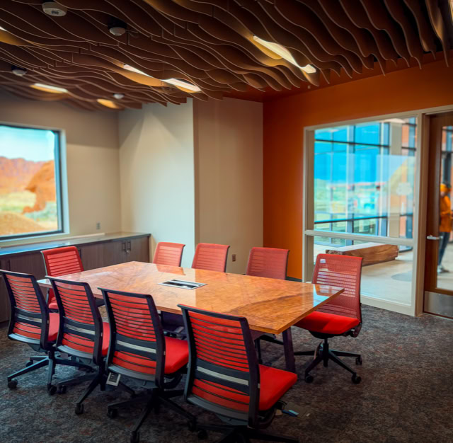 A conference room with a Stone table surrounded by red chairs, a window showing an outdoor view, and a glass door with a person visible outside. At the Valley Of Fire in las vegas nv.