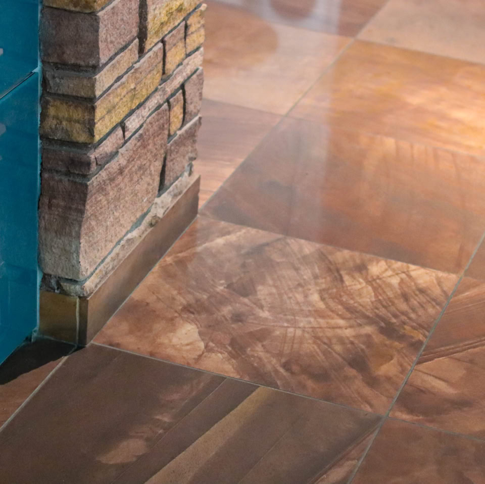 Shiny brown tiled floor with a reflection, adjacent to a blue wall and a brick column.