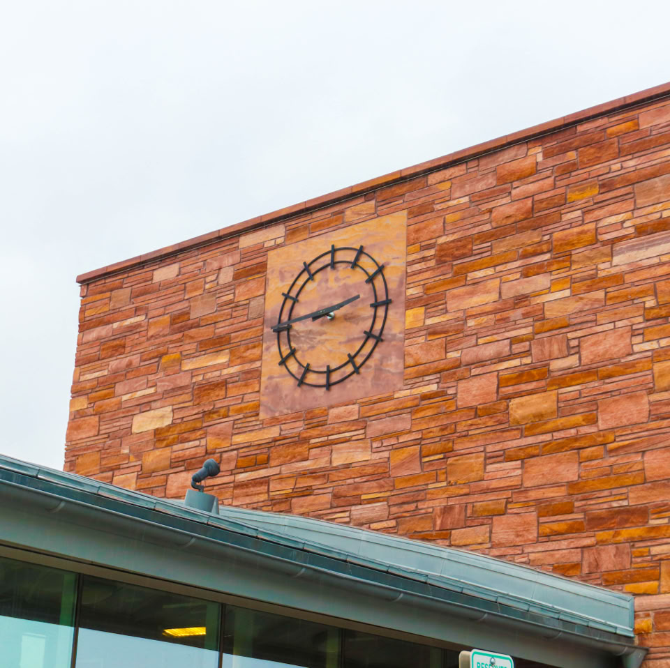 A brick building facade with a large clock on it, adjacent to a modern glass structure.