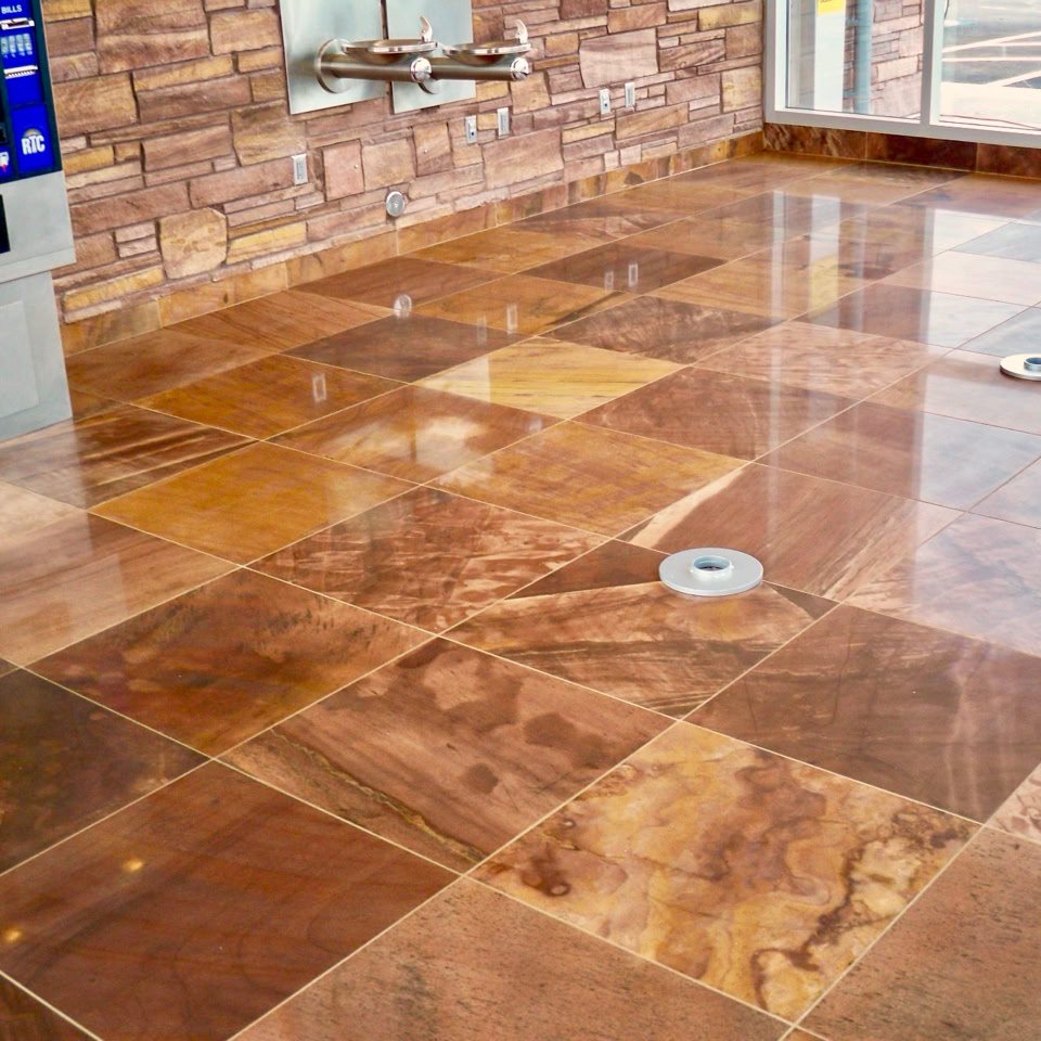 Polished brown and tan tiled floor in a room with a stone wall and a vending machine.