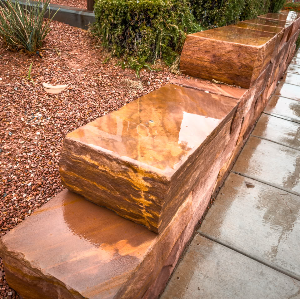 Wet stone benches next to a paved walkway, with mulch and greenery in the background.