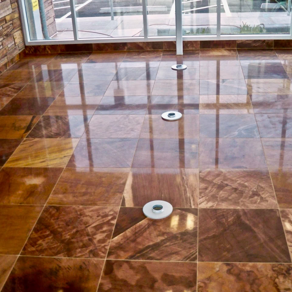 Shiny brown tiled floor with circular drains, surrounded by glass walls and cleaning equipment in the corner.
