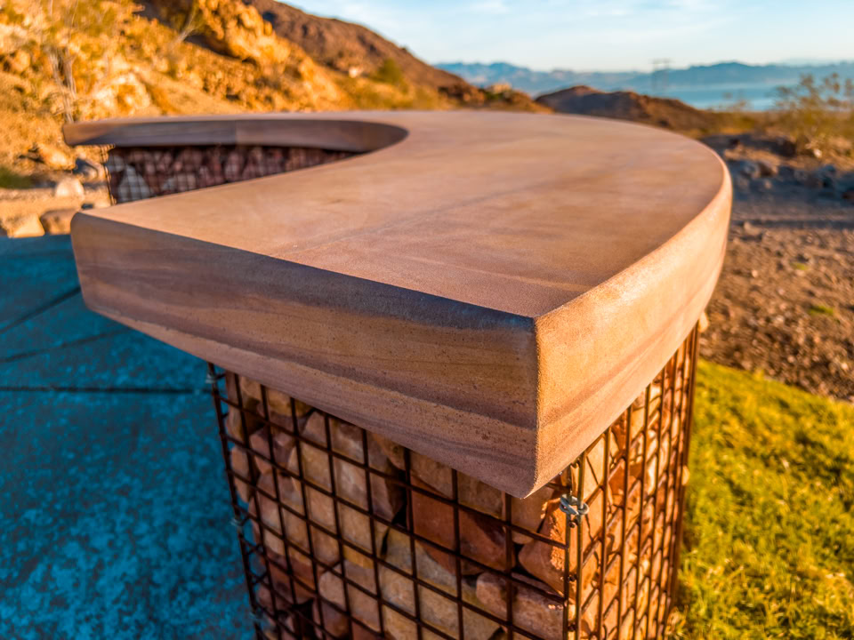 Curved wooden bench on a stone base with a mountainous landscape in the background.
