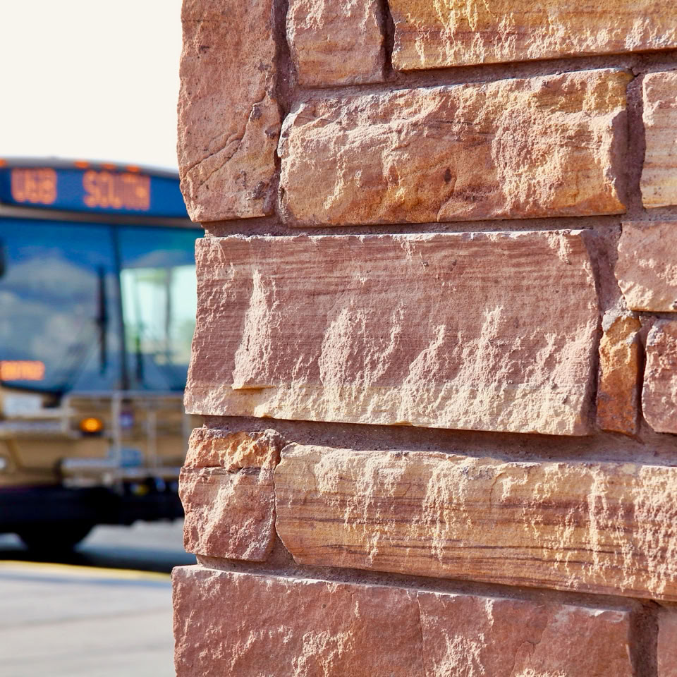 A brick wall in the foreground with a blurred view of a bus in the background.
