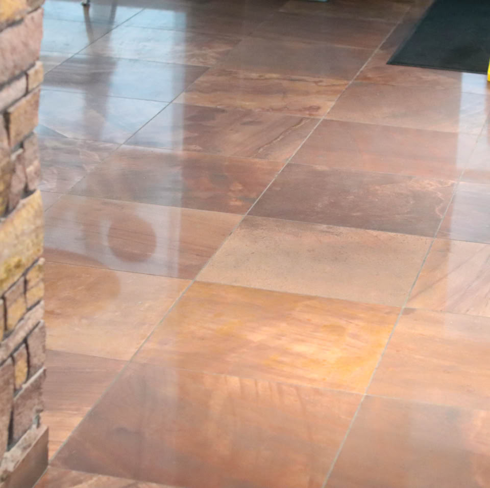 Shiny tiled floor with a stone pillar on the left and a yellow caution sign in the background.
