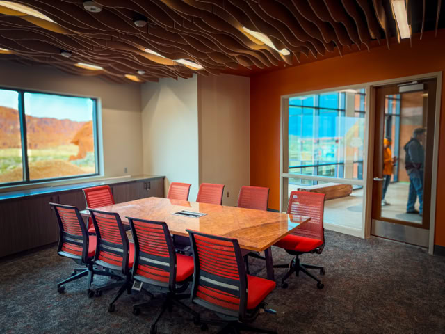 A conference room with a Stone table surrounded by red chairs, a window showing an outdoor view, and a glass door with a person visible outside. At the Valley Of Fire in las vegas nv.