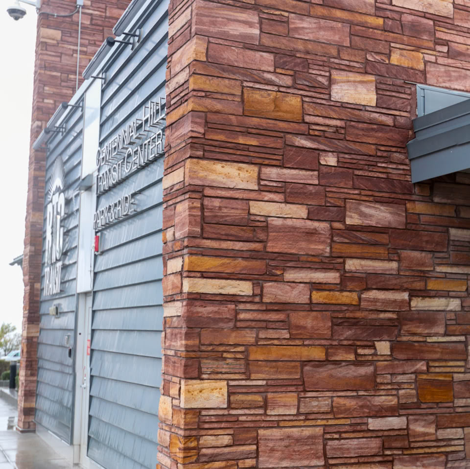 A building exterior with a combination of red brick and gray siding, featuring a wet concrete walkway in the foreground.