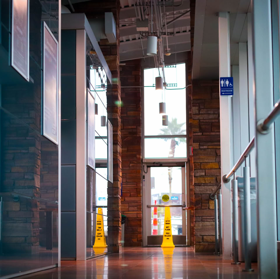 A hallway with large windows, reflective floors, and yellow caution signs.